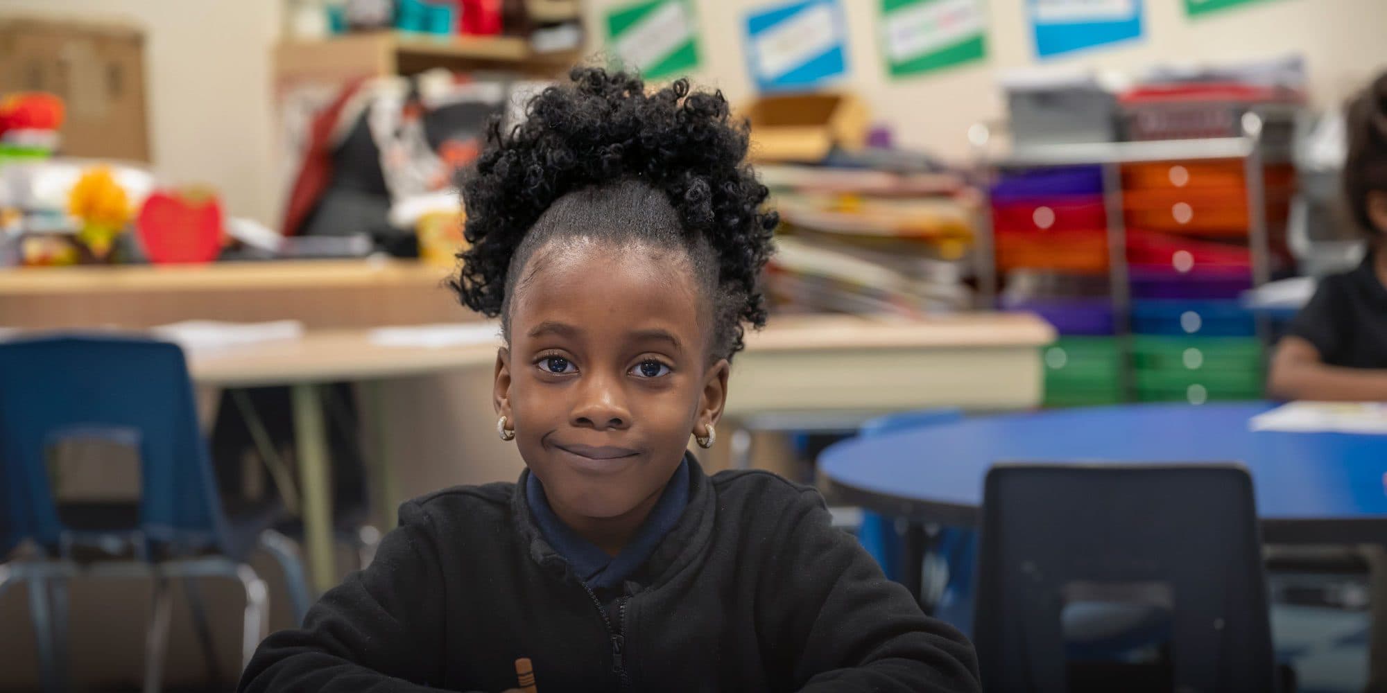 Smiling student working at a desk in a classroom.