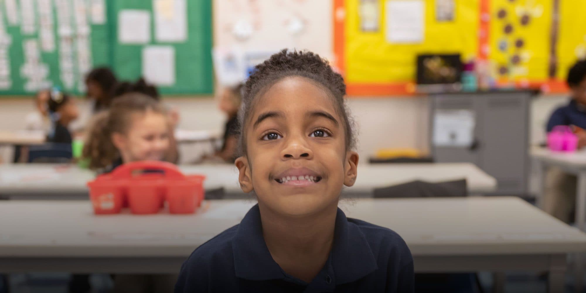 Smiling elementary student sitting at a desk in a classroom.