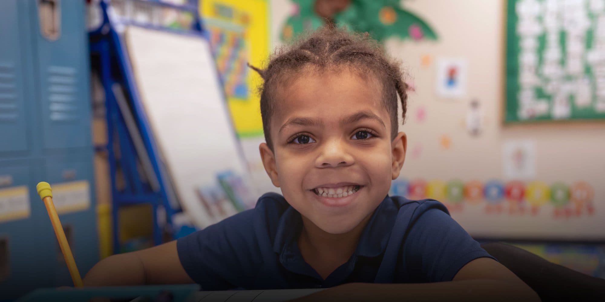Smiling elementary student writing at a desk.