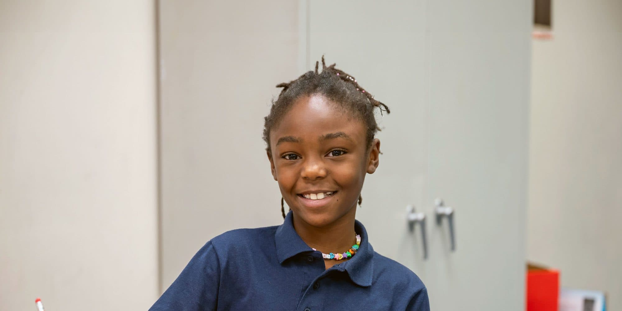 Smiling student with braided hair and a colorful beaded necklace.