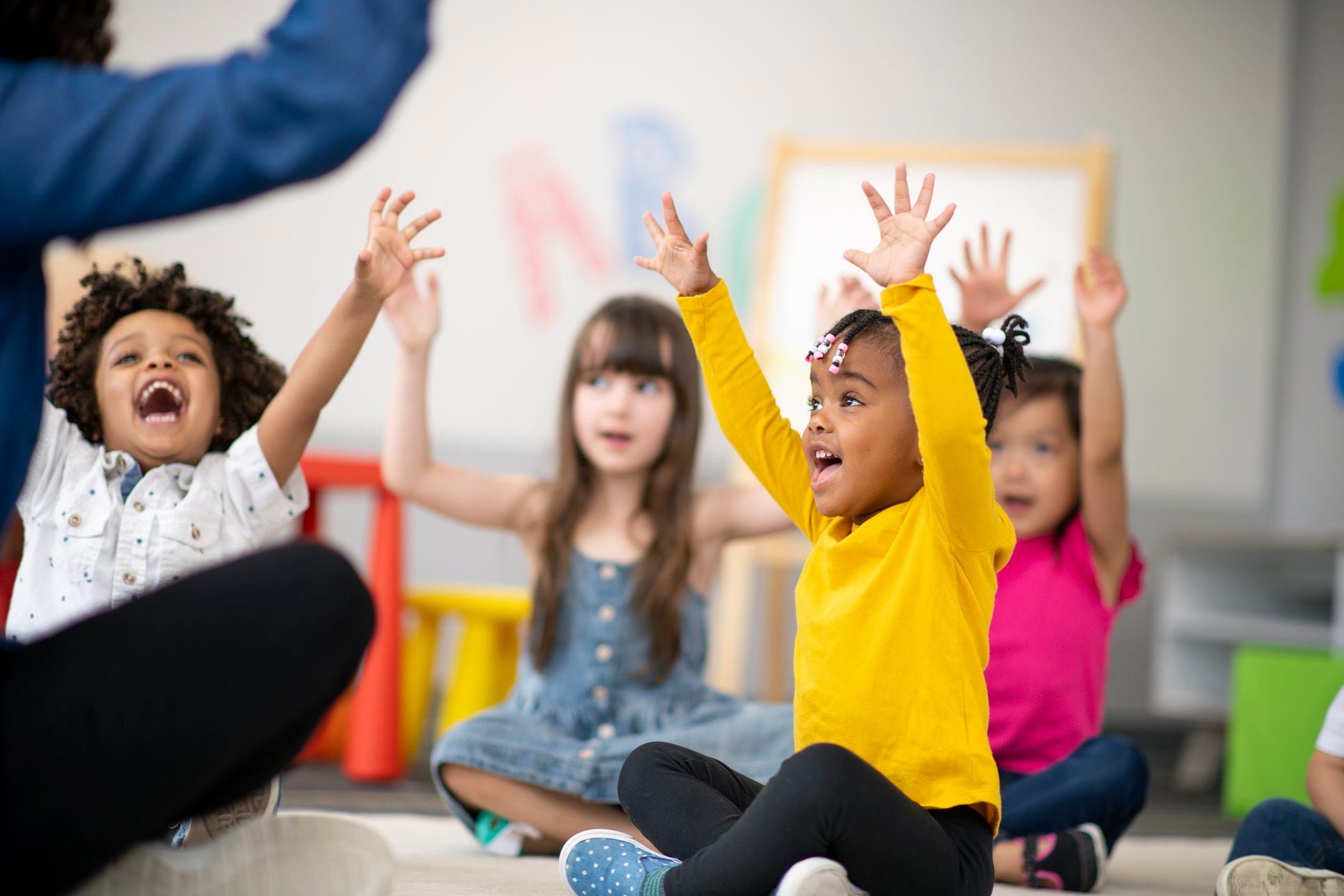 Happy children with raised arms in a classroom.