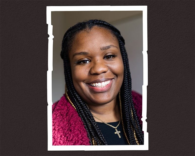 Smiling adult with braided hair and cross necklace in a photo frame.